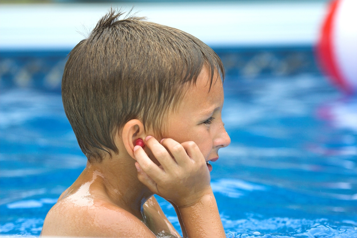 Young boy touches ear plug while swimming