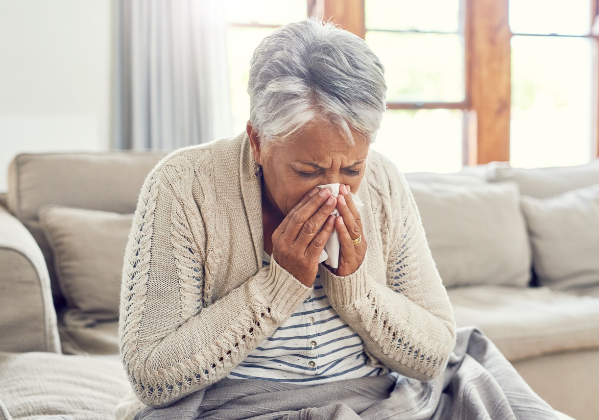 Senior woman on her couch sneezing into a tissue.