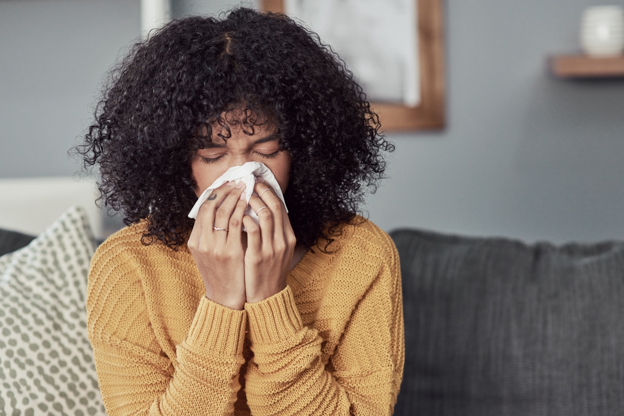 Woman with the flu blowing her nose into a tissue.